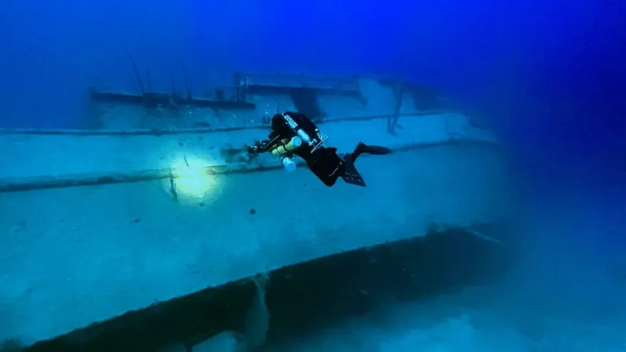 A rebreather diver gliding over the Josie J wreck in deep blue water